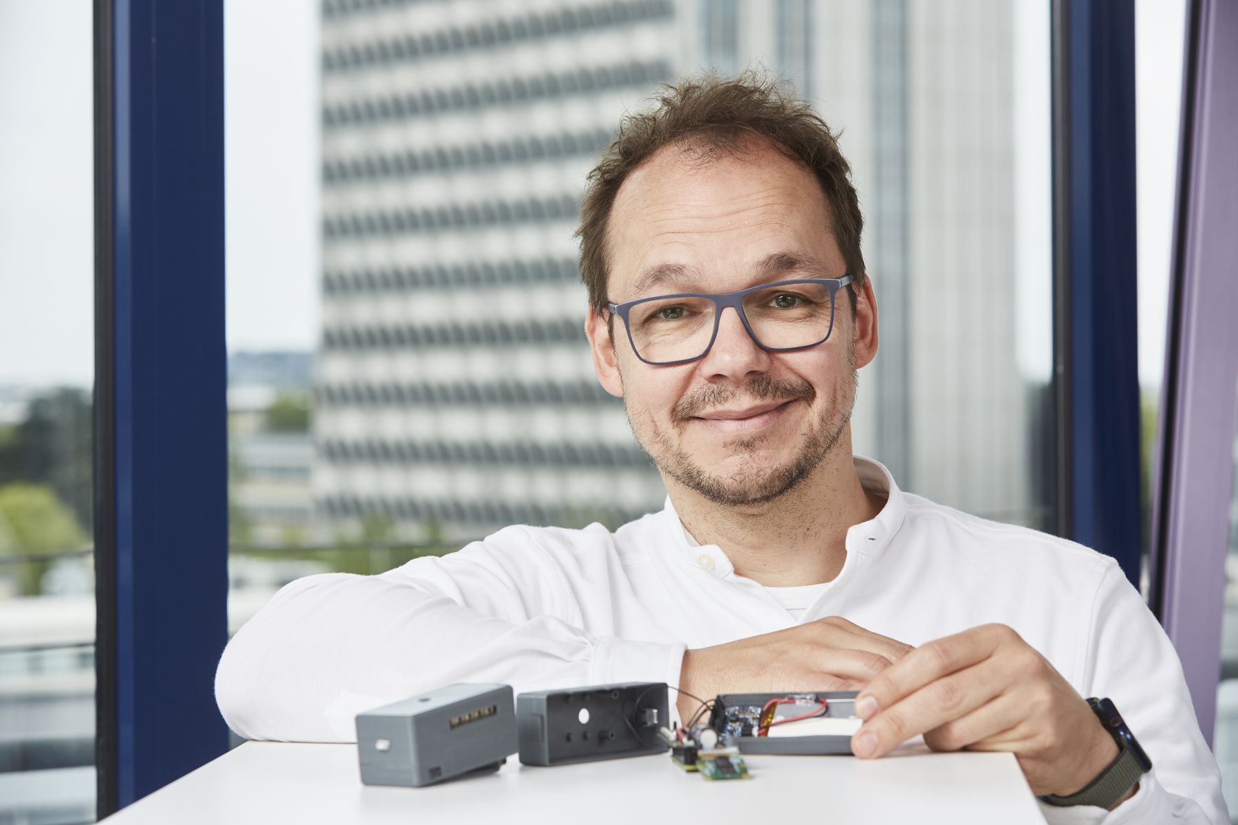 Portraitfoto von Prof. Zahout-Heil in seinem Büro. Auf seinem Tisch liegt die von ihm entwickelte Lesehilfe, im Hintergrund sieht man unscharf das h_da-Hochhaus. 