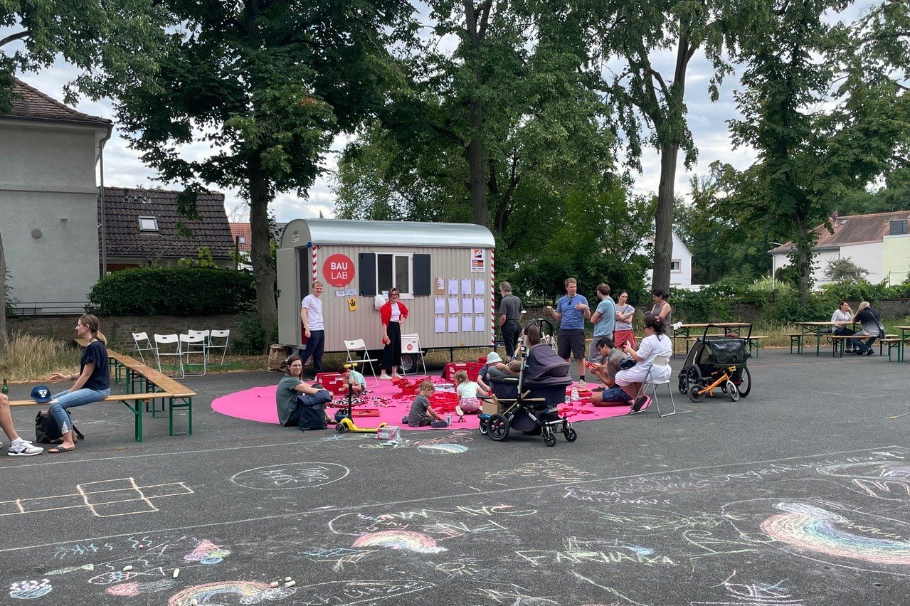 Studierende an Tischen und auf Sitzdecken vor dem Bauwagen des BAULAB