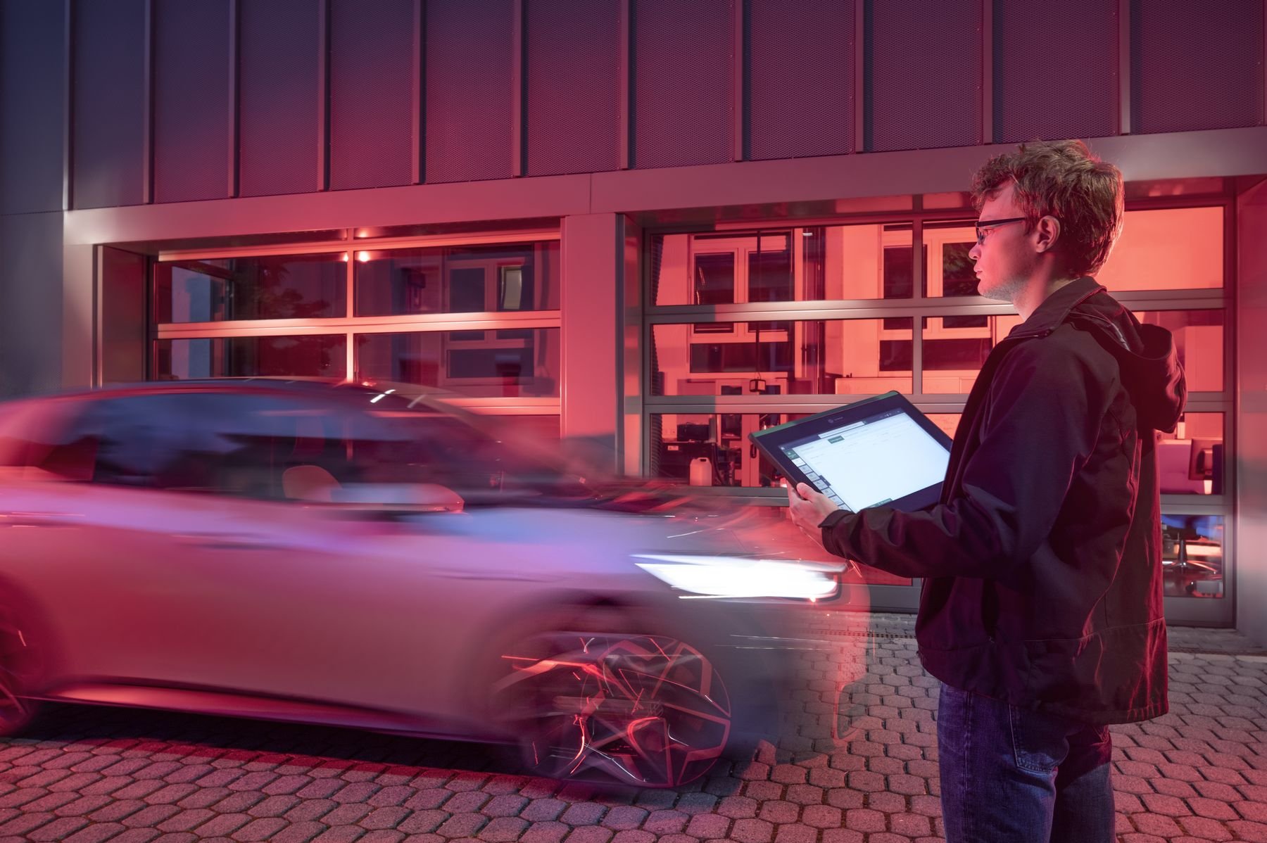 Ein Mann steht mit Laptop auf der Straße, während ein Auto vorbeifährt.