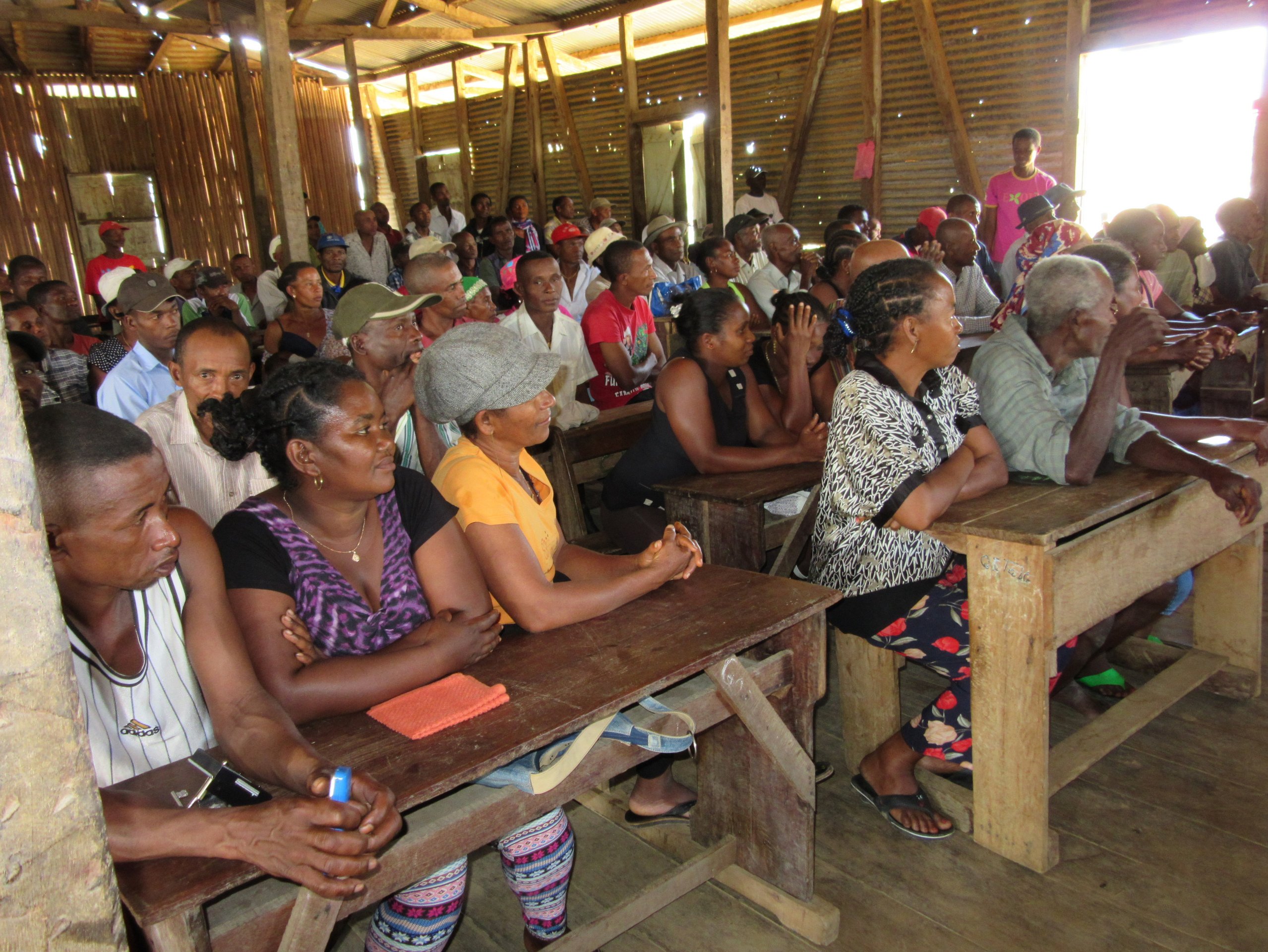Vanillebauern und Vanillebäuerinnen auf Madagaskar sitzen bei einer Veranstaltung auf Schulbänken. 
