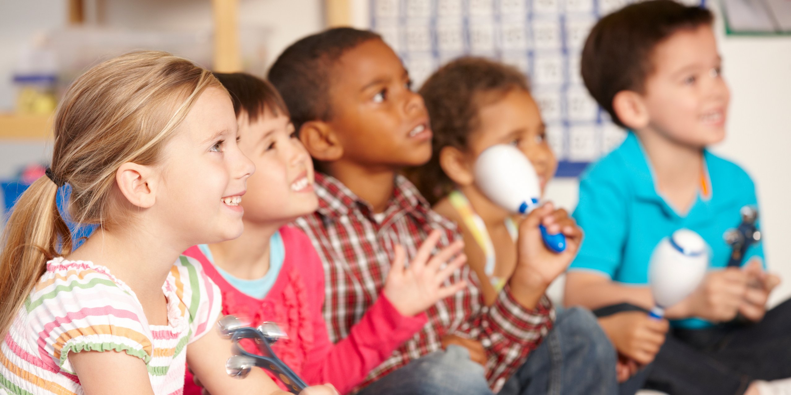 Bunt gemischte Kindegruppe auf dem Boden sitzend beim Musizieren