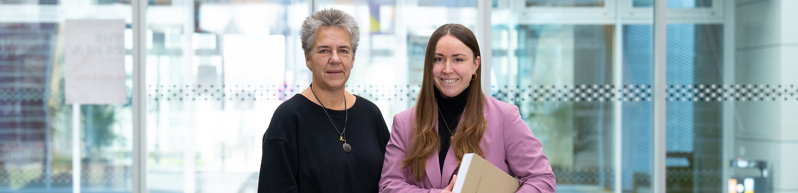 Promovendin Renee März und ihre Betreuerin Prof. Yvonne Haffner nebeneinander vor Glastüren auf dem Campus 