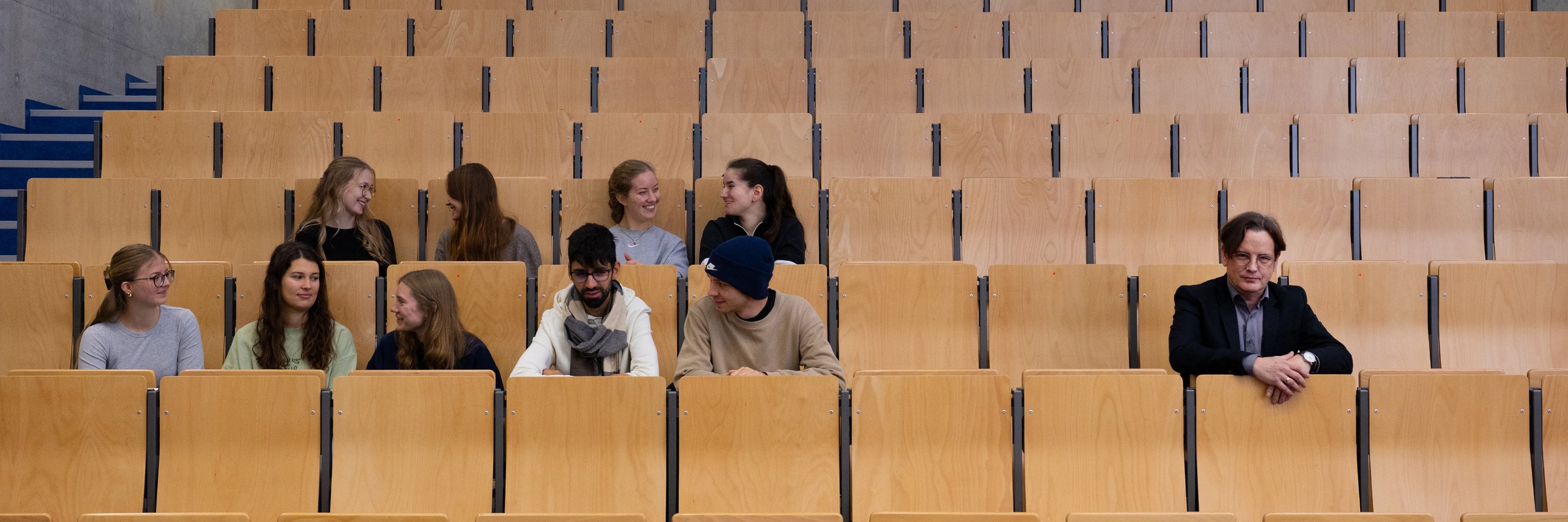 Studierende sitzen als Gruppe in einem Hörsaal, rechts davon Professor Mario Rund