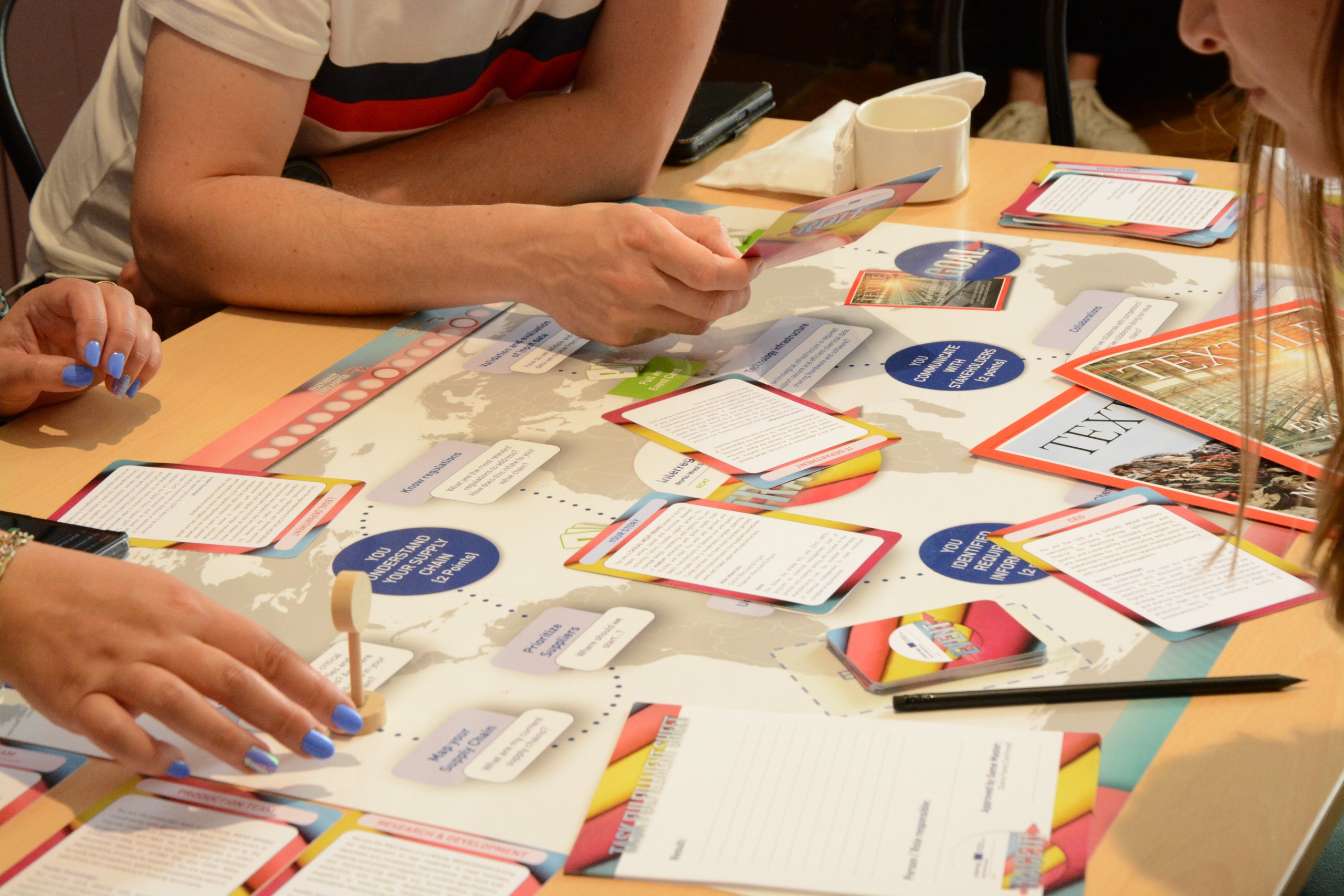 Tisch mit einem großen Spielfeld darauf, Hände, die Textkarten halten und Spielfiguren über das Feld führen