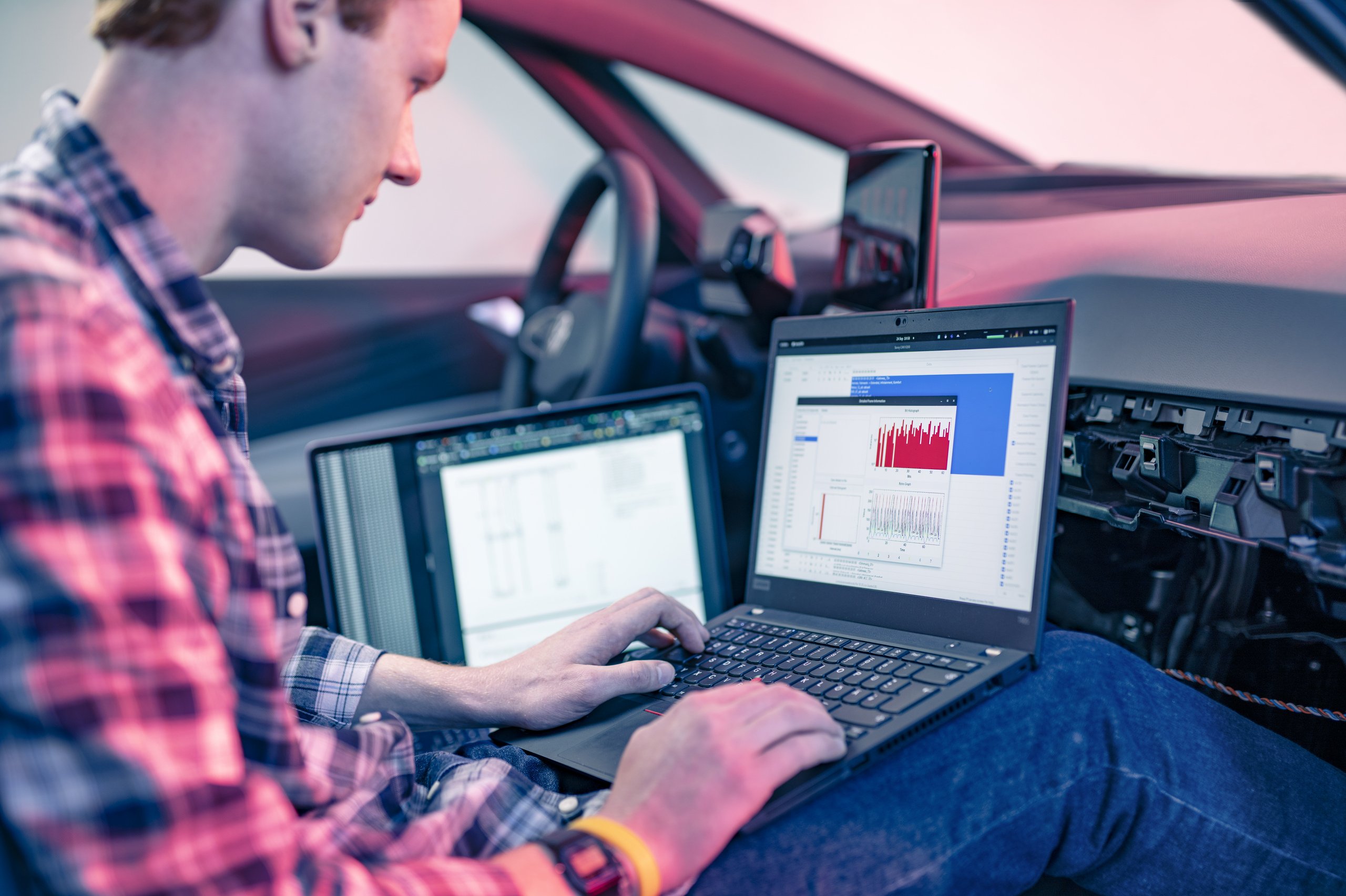 Ein Mann sitzt mit aufgeklapptem Laptop in einem Auto.
