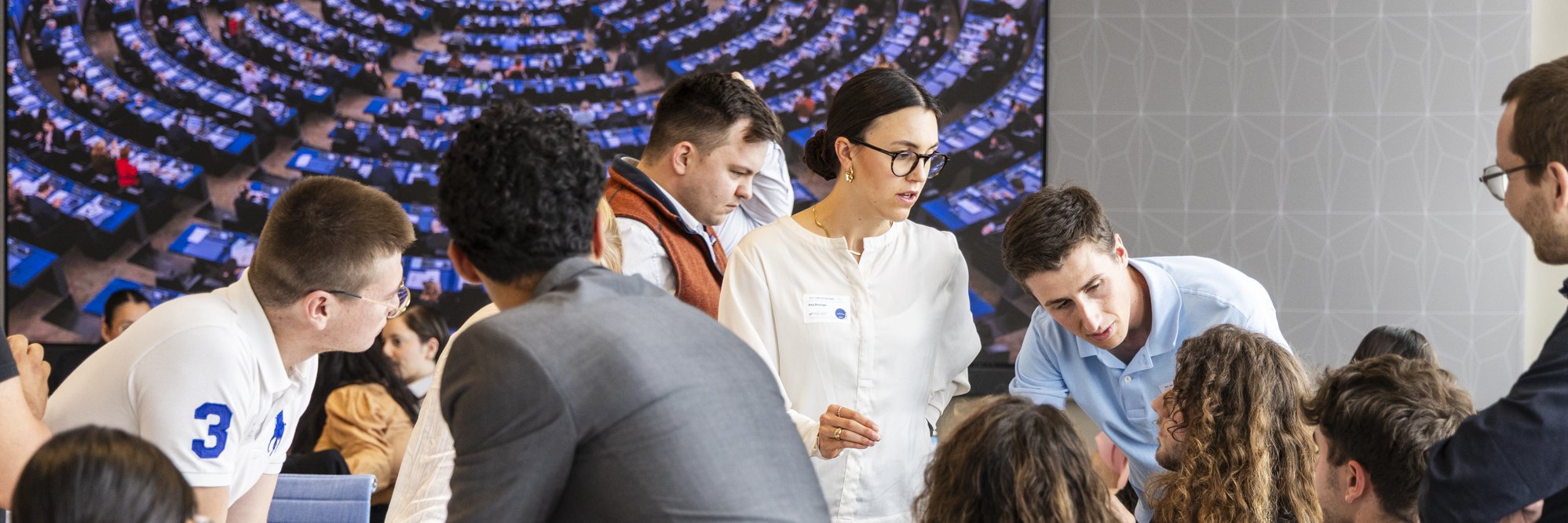 Gruppe von Studierenden im h_da Senatssaal, im Hintergrund auf einem Screen der Plenarsaal der EU-Parlaments