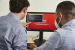 Two men look at a computer screen where a ransomware message appears.