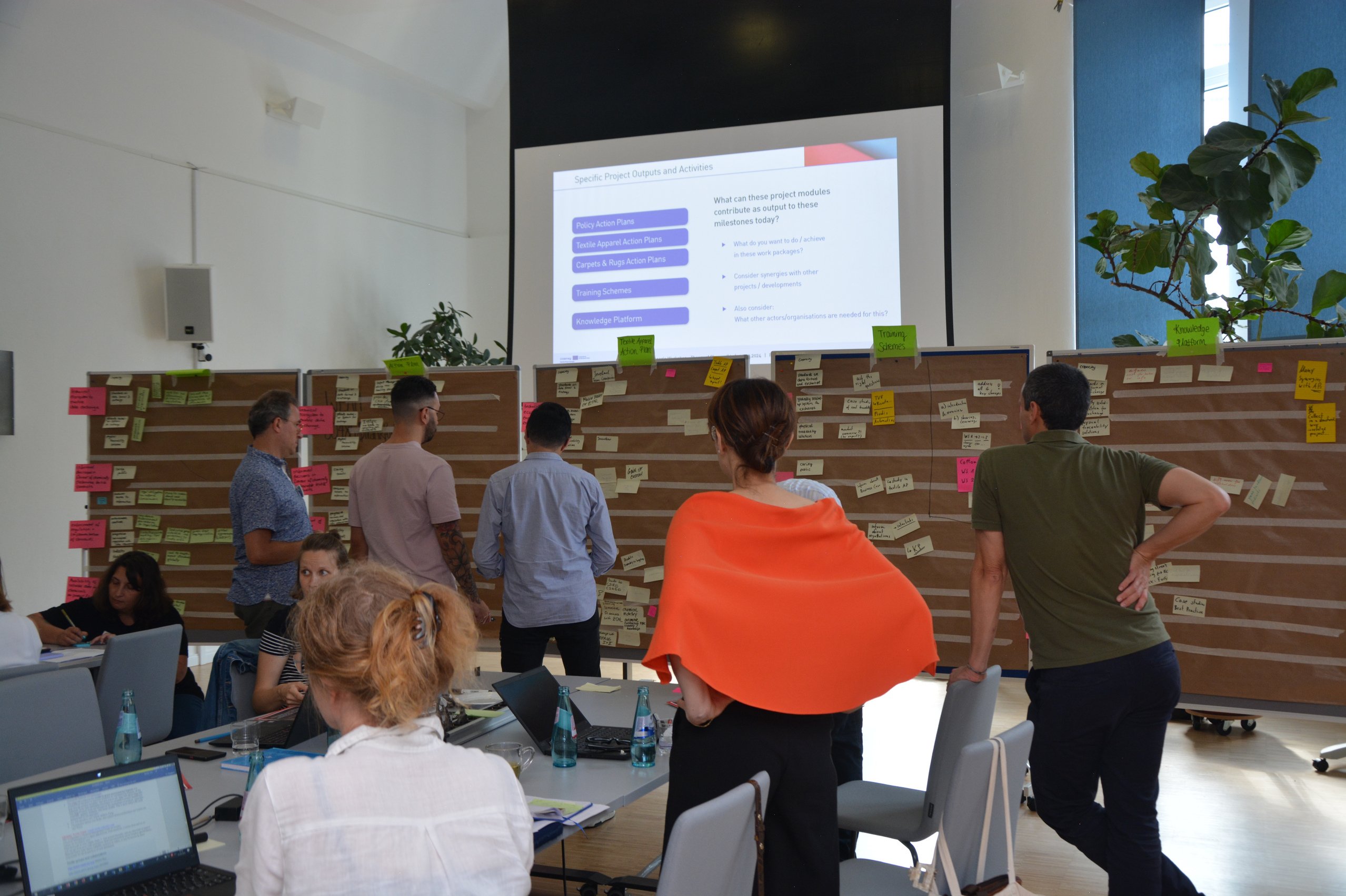 Workshopsituation mit Pinnwänden mit unzähligen Post-its daran und Menschen davor