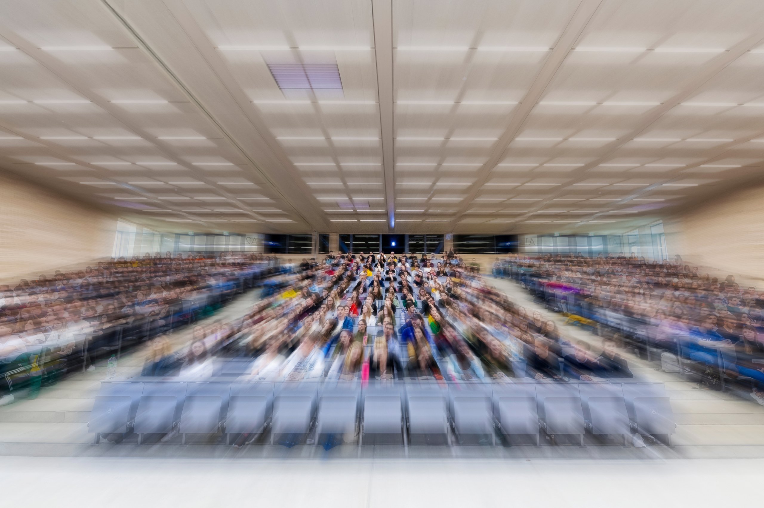 Verschwommene AUfnahme eines Hörsaals mit vielen Studierenden in SItzreihen