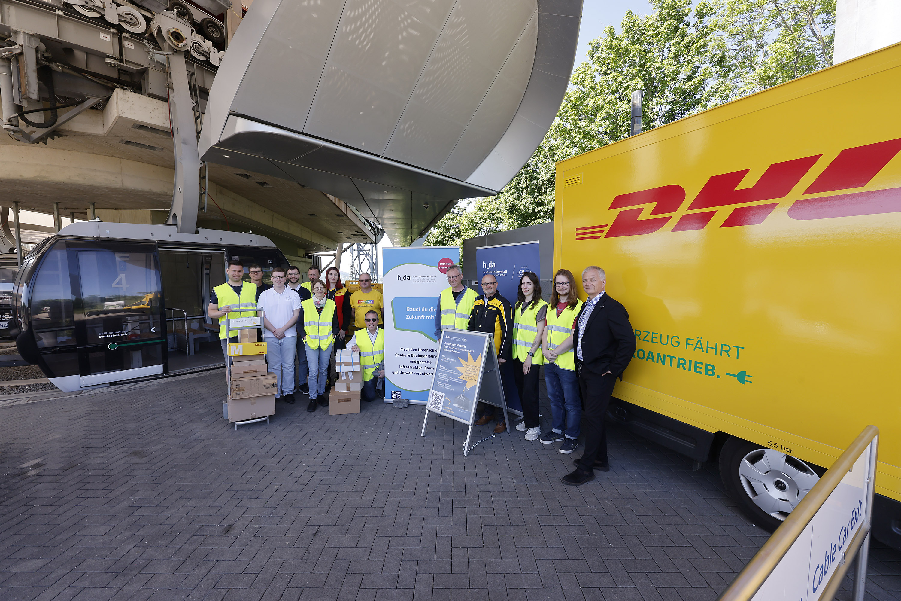 Projektgruppe mit gelbem DHL-Transporter an der Seilbahnstation