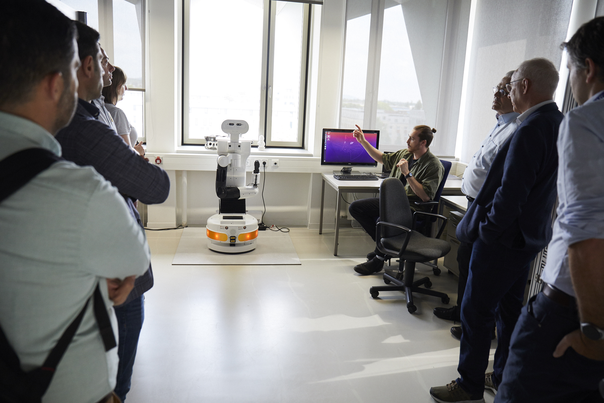 Tiago-Roboter vor einem Fenster im Labor, rechts und links Menschen, die ihn betrachten