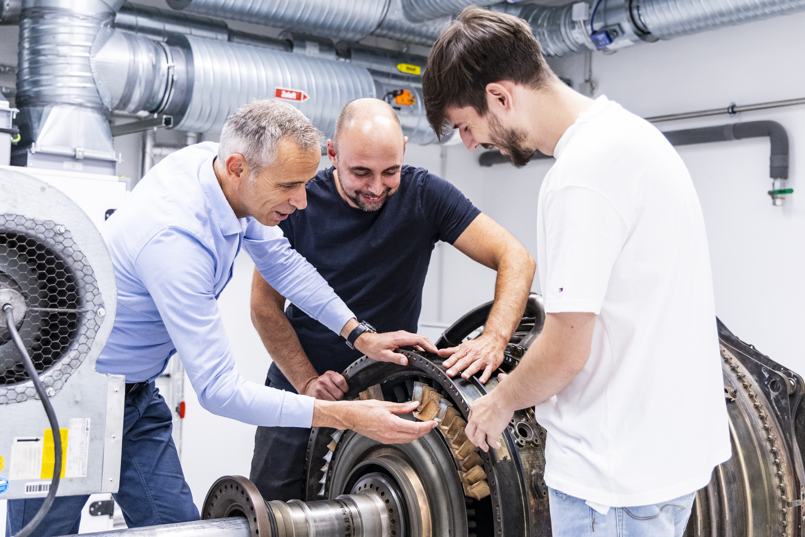 Dreierteam beugt sich in der Turbinenhalle bei der Arbeit über ein Bauteil