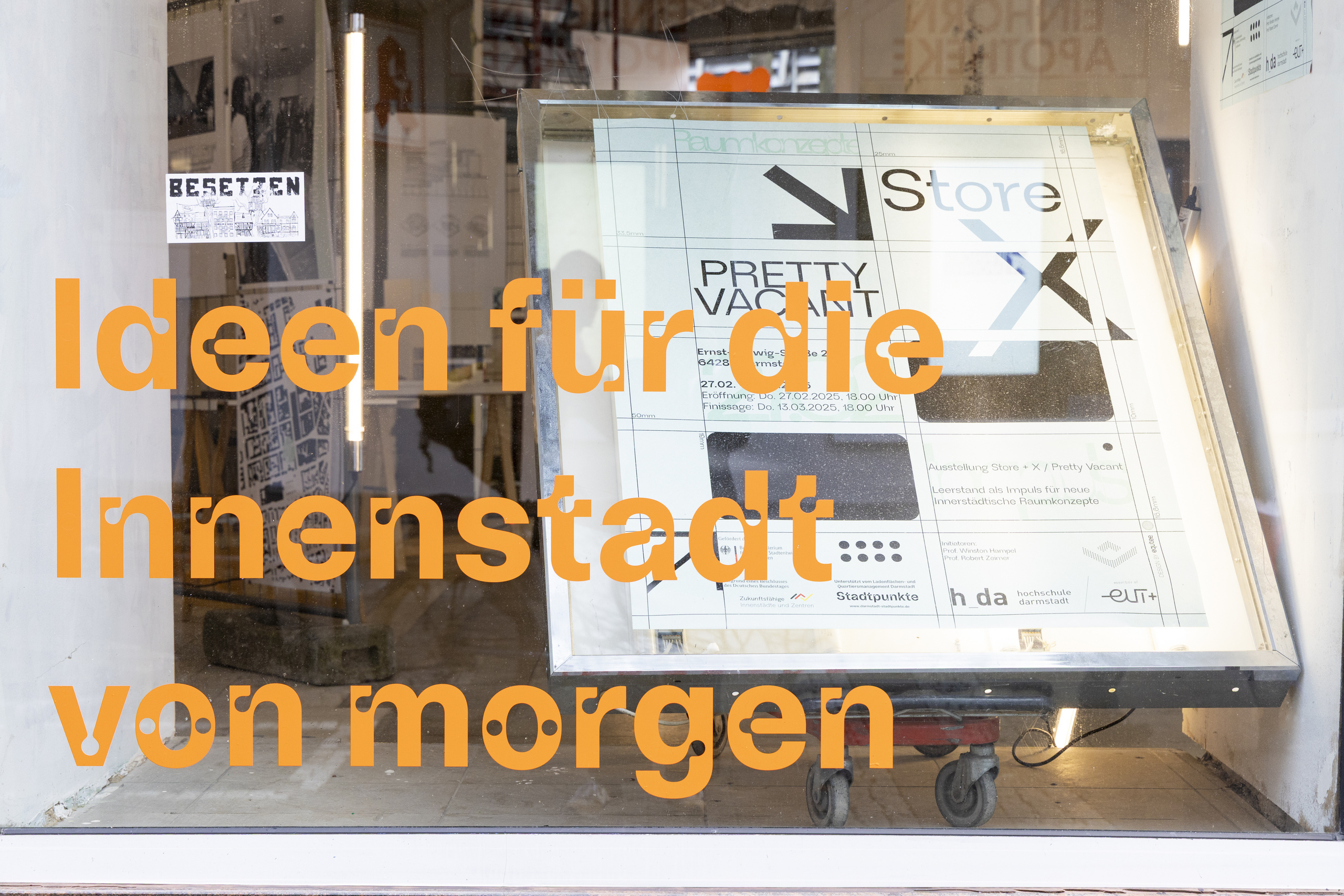 Blick von außen durch beschriftete Fensterscheibe in den AUsstelungsraum