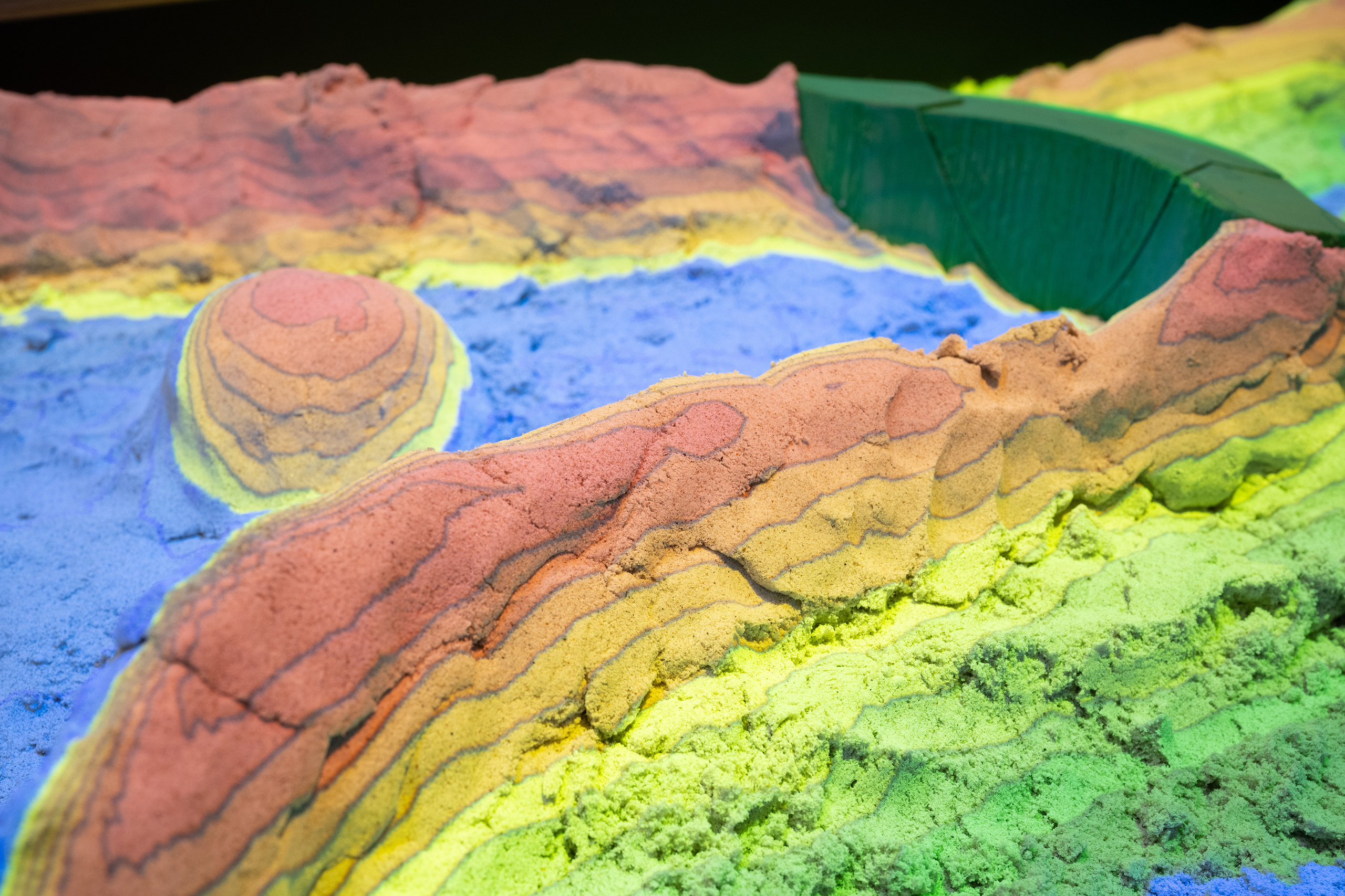 Blick in die Sandbox, in der aus Sand ein Fluss mit einem Staudamm modelliert ist.